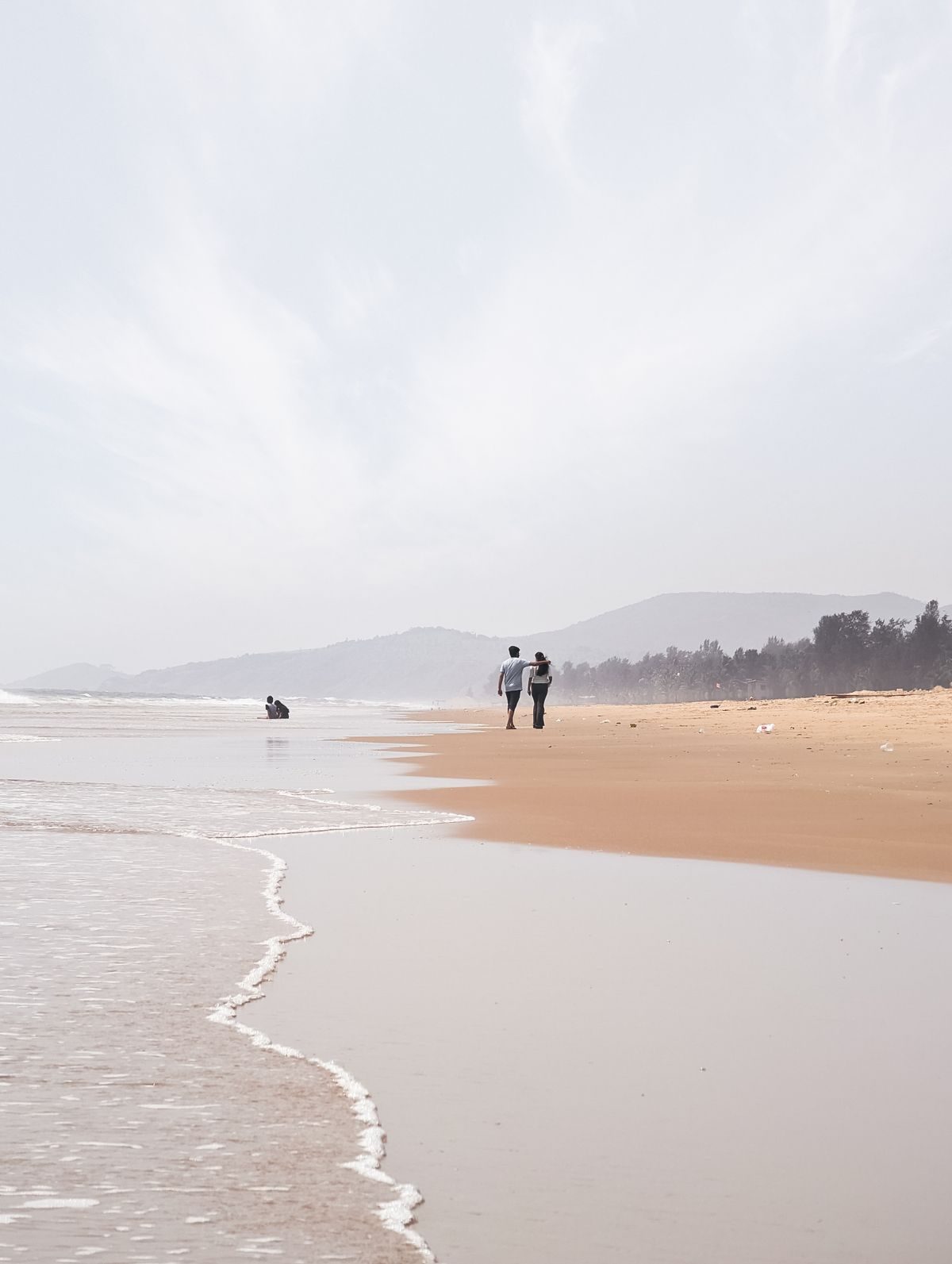 Couple walking on a quiet Kundapura beach at low tide